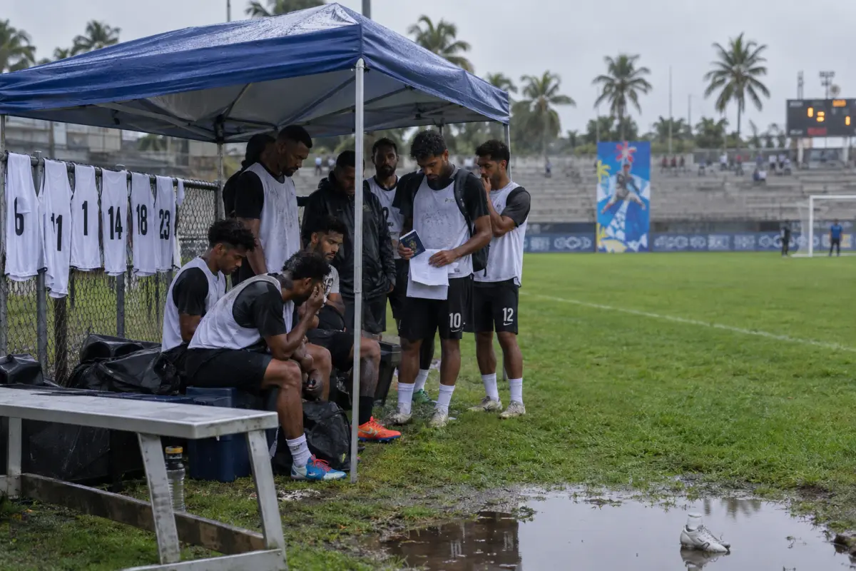 Players wait under a tarp on the training pitch in Suva after late eligibility rulings left squads short of registered players.