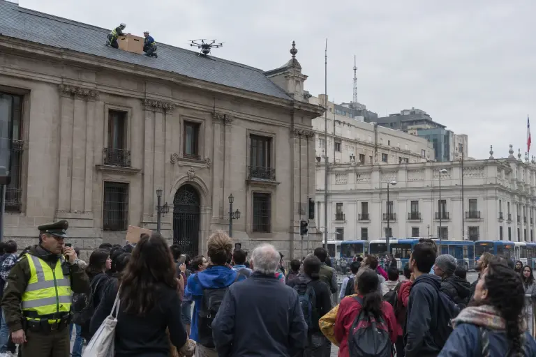 Protesters and police watching as a protest drone rests on the roof of the Chamber of Deputies, Plaza de la Constitución, Santiago.